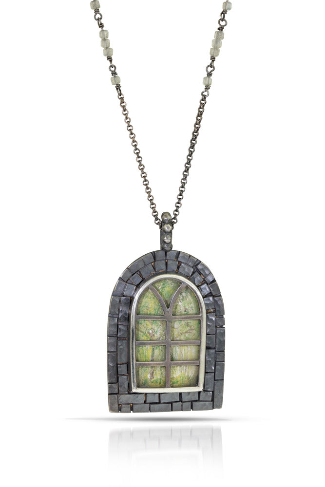 A rounded arch window necklace in oxidized sterling silver, with crystal quartz  as window panels and woody green tree drawings on background. Blacked finished textured "bricks" frame the window. On oxidized sterling silver rolo chain with labradorite cute accents.