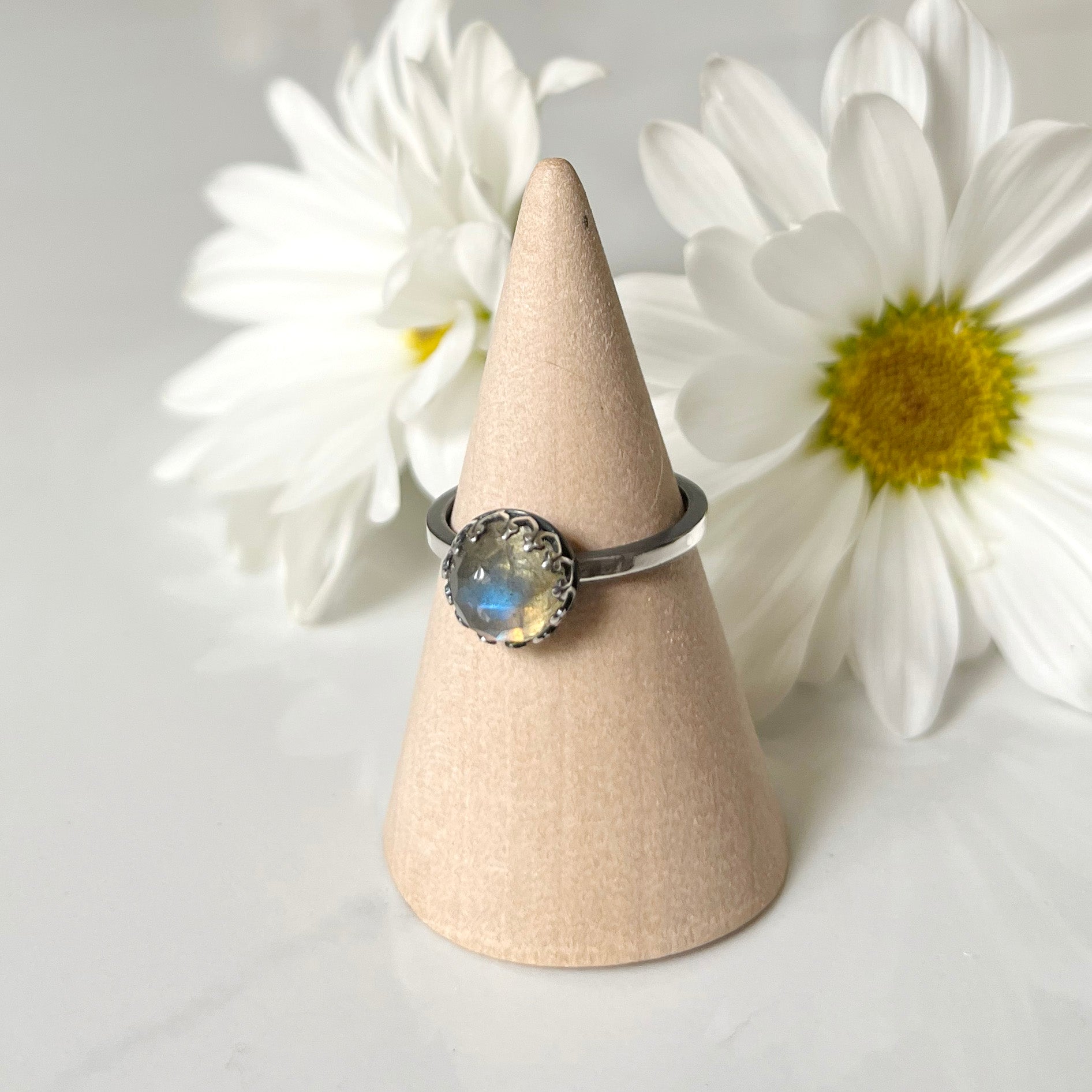 Flashy 8mm round rose cut labradorite stone set into fancy sterling silver setting, on oxidized sterling silver straight band with notch details. White daisies in background.