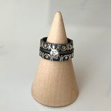 Set of 3 stacking ring set with one initial ring in center sandwiched with two trellis bands, which showcase continuous shiny silver motif relieved against blackened finish.