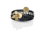 A set of three rings, including one golden four petaled flower in 14k gold on oxidized silver band, one small gold coin in 14k gold with an initial A stamped on, and one oxidized sterling silver beaded band with highlighted dots. 