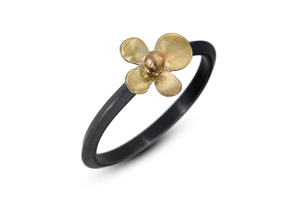 A four petaled delicate flower in 14k solid yellow gold sits on top of oxidized sterling silver band, for casual or formal occasions. Image by Cole Rodger